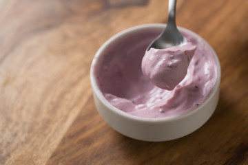 eating blueberry yogurt from white bowl on wood table