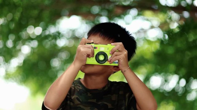 Little boy takes photo with toy camera on green bokeh background