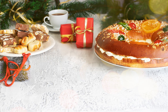 Spanish Christmas concept , Roscon de reyes  or Spanish holiday cake with hot chocolate, sweet coal  and turrones candies, red Christmas gifts on white background .Copy space