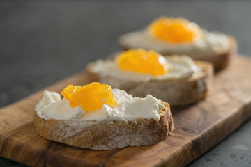 Three ciabatta slices with ricotta and orange marmalade on olive wood board on terrazzo surface