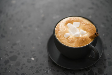 cappuccino with marshmallow and cinnamon in black cup on terrazzo surface with copy space