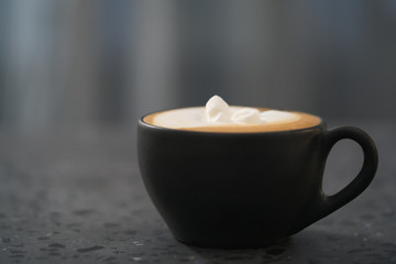 cappuccino with marshmallow in black cup on terrazzo surface with copy space