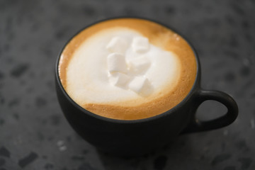 cappuccino with marshmallow in black cup on terrazzo surface