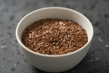 Flax seeds in white bowl on terrazzo surface closeup