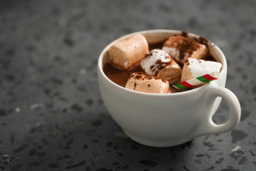 Cocoa drink with marshmallow and christmas drinking straw in white cup on terrazzo surface with copy space