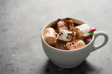 Cocoa drink with marshmallow and christmas drinking straw in white cup on terrazzo surface with copy space