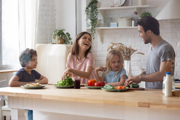 Cheerful family with kids preparing vegetable salad in domestic kitchen