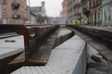construction of tracks for trams in the old town. rusty rails close-up, city and construction workers in yellow vests are blurred in the background. repair of roads