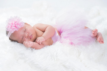 Cute newborn baby wears a pink flower crown lies swaddled in a white blanket.