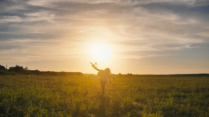 Obraz na płótnie Canvas A young girl runs with a toy airplane against the sunset sky.