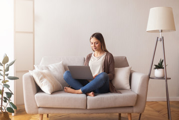 Cute young girl surfing in internet on laptop, resting on couch