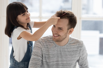 Caring happy preschool daughter brushing combing father hair.