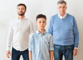 Boy Standing Between Father And Grandfather Next To Wall Indoor