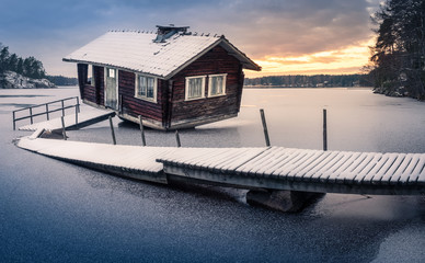 Abandoned sauna and broken pier with sunset landscape at winter evening in Finland