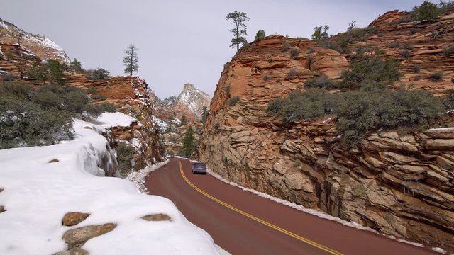 Car driving on winding road through winter landscape in Zion as it goes through small canyon.