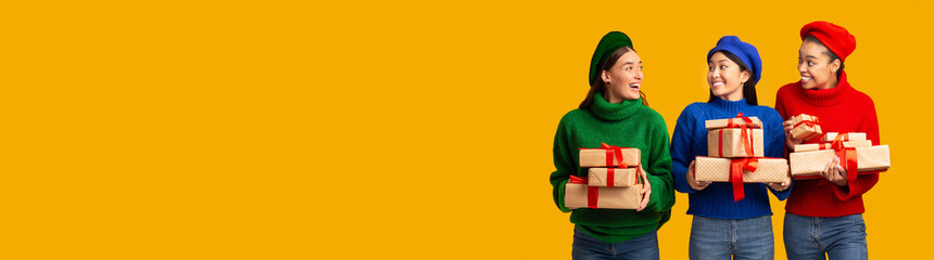 Three Girls Holding Gifts Standing In Studio Over Yellow Background