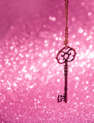 Fototapeta na wymiar vintage golden key on blurred glittering pink abstract background. creative concept of secret love, key of happiness, Valentines day. copy space