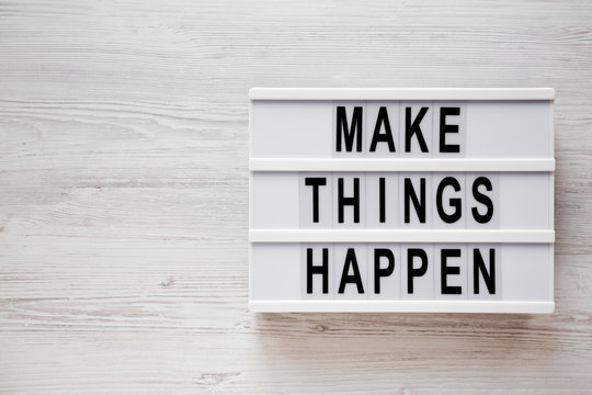 'Make things happen' words on a lightbox on a white wooden background, top view. Overhead, from above, flat lay. Copy space.