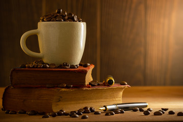 Coffee bean in the white cup and vintage book stacking on wooden table in morning light.