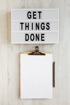 'Get things done' words on a modern board, clipboard with blank sheet of paper on a white wooden surface, top view. Overhead, from above, flat lay.