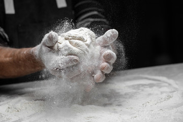 Hands baker preparing yeast dough with white dust flour on black background, scoop for pasta and pizza
