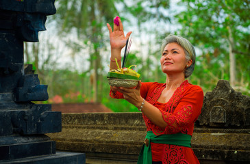 beautiful and happy Asian Indonesian woman dressed in traditional Balinese religious custom holding...