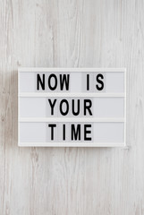 'Now is your time' words on a modern board on a white wooden background, top view. Overhead, from above, flat lay.