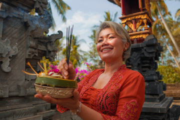 beautiful and happy Asian Indonesian woman dressed in traditional Balinese religious custom holding...