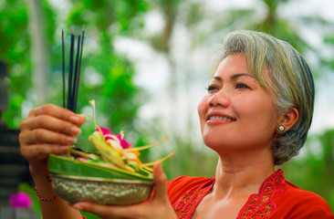 beautiful and happy Asian Indonesian woman dressed in traditional Balinese religious custom holding...