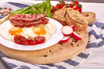 fried eggs on a wooden table, accompanied by fresh green parsley, cherry tomatoes on a branch, with fried crispy bacon and toasted baguette.