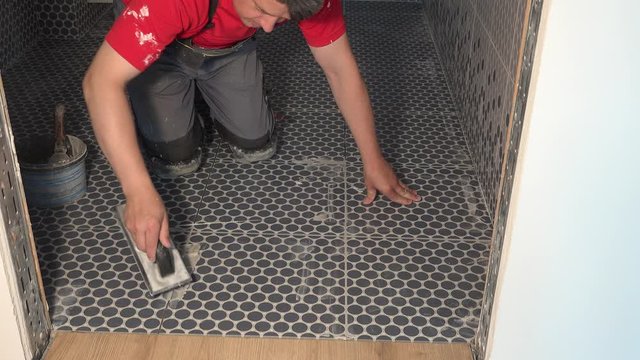 Skilled worker putting fugue on floor tiles in bathroom. Grouting ceramic tiles