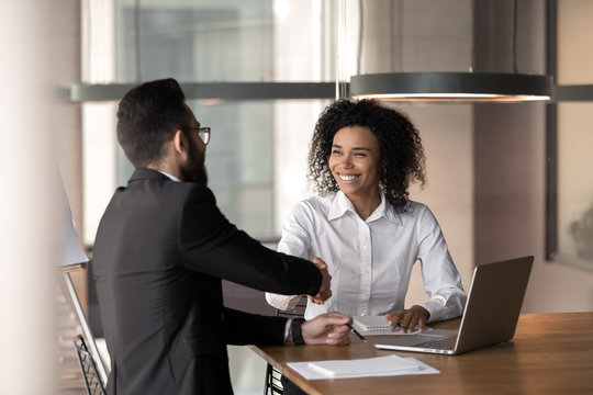 Smiling diverse business partners handshake closing deal at meeting