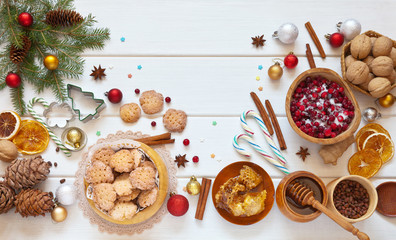 Traditional Christmas sweets: homemade cookies, sugar cranberries, honeycombs, nuts and candy canes on a white table with decorated Christmas tree branches. Flat lay, copy space