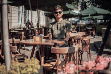 Handsome man sits in cozy cafe in old city. Wooden tables and chairs in an outdoor cafe