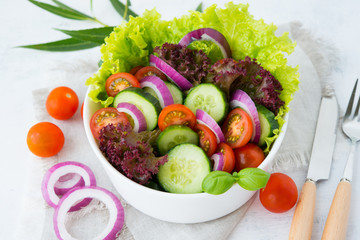 Fresh vegetable salad on white background close. Dinner of lettuce, tomatoes, onions and cucumbers.