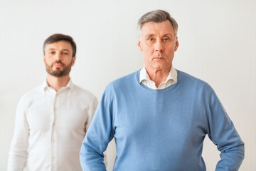 Mature Son Standing Overshadowed By His Elderly Father, White Background