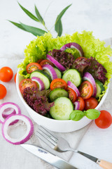 Fresh vegetable salad on white background close. Dinner of lettuce, tomatoes, onions and cucumbers.