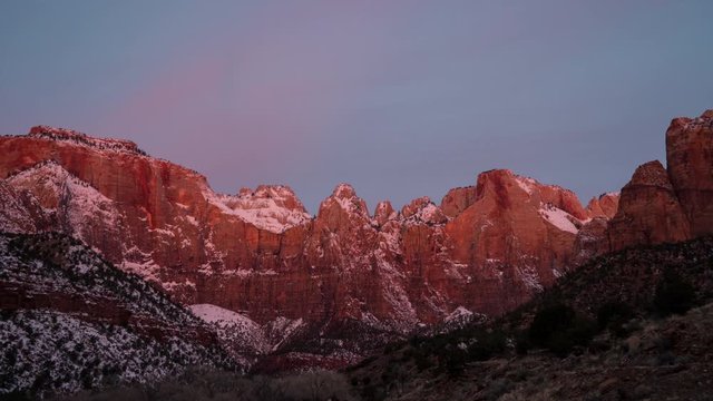 Timelapse of the cliffs in Zion lighting up during colorful sunrise as the colors change on the walls and clouds.