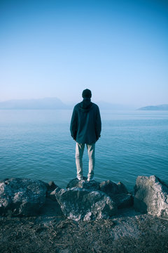 solitude man concept, depressed emotions of a person that stands alone on the shore looking the lake