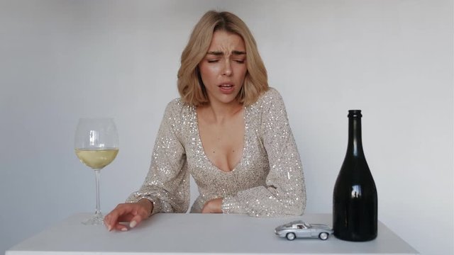 Do not drink and drive concept. Woman with bottle and glass of wine on white background is played with car toy