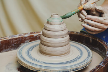 Hands on pottery wheel. Craftsman artist painting pot with brush