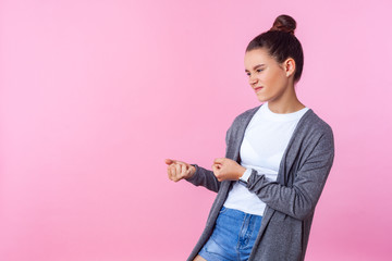 Portrait of persistent brunette teenage girl with bun hairstyle in casual clothes pretending to pull with big effort, diligent expression. indoor studio shot isolated on pink background, copy space
