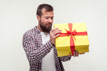 Portrait of frustrated sad bearded man in casual plaid shirt unpacking present with dissatisfied frowning face, displeased with bad gift, spoiled holidays. studio shot isolated on white background