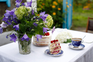 Obraz na płótnie Canvas Homemade cake and a bouquet of flowers on a table in a summer garden
