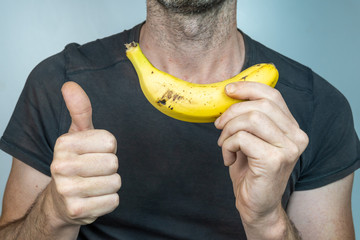 Young caucasian man with banana in his hand and thumb up on isolated White background