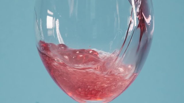 Wine coctail with ice in a glass. Red wine coctail pouring in a glass over blue background. Rose wine pour into a glass. Close up shot. Slow motion 