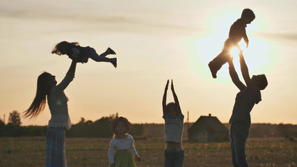 The concept of a happy large family. Happy parents tossing their children up on a sunset background.