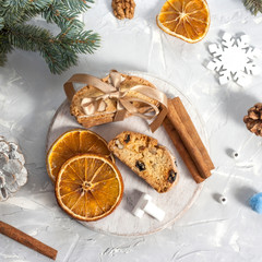 Traditional Italian biscotti or cantuccini cookies on a round white wooden board with cinnamon, dried orange slices and marshmallows on a light table near a Christmas tree. Christmas baking concept