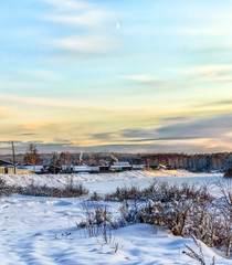 Winter landscape. The new moon hovered over the village. Cold. Stoves are heated in houses. Smoke is coming from the chimneys. December.Vertical photo