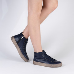 Classic leather high top sneakers for women. Photo on legs of a model on a white background